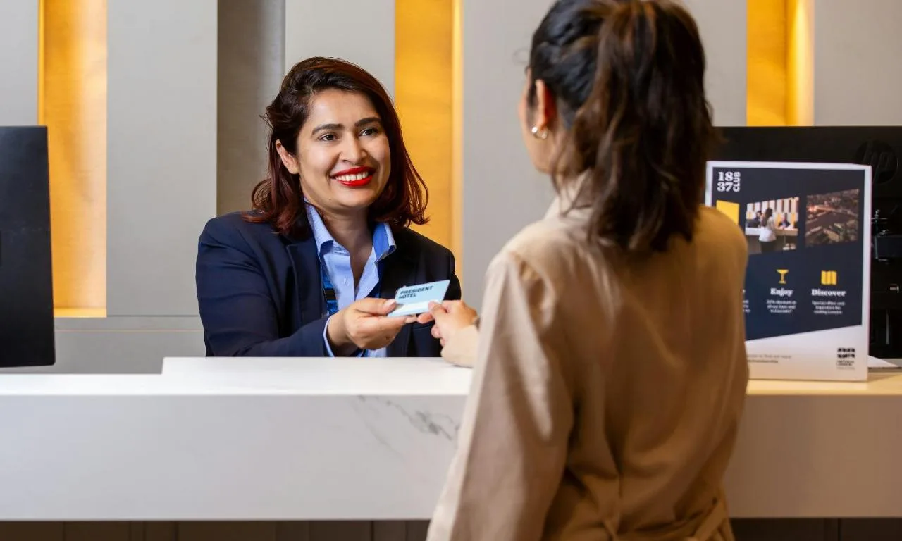 a woman standing at a counter holding a credit card at President Hotel in London